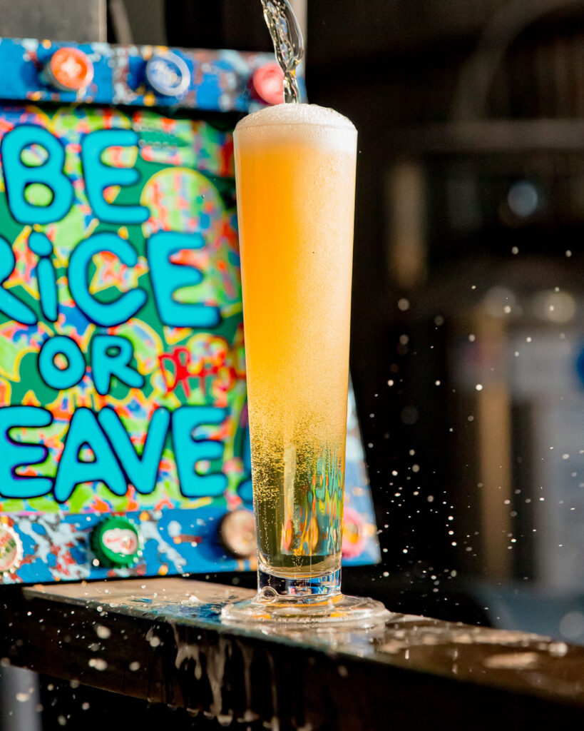 a tall lager glass of be rice or leave beer with a handpainted sign by dr. bob art